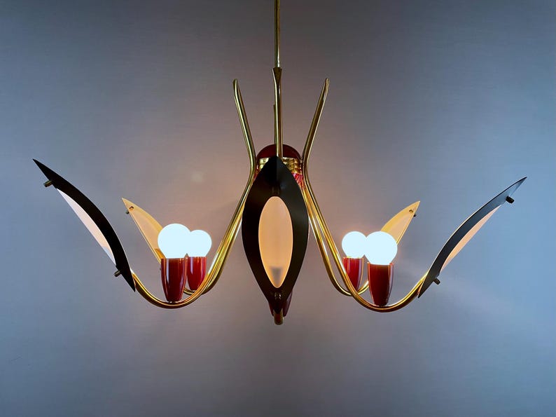 May include: A mid-century chandelier with a gold-tone frame, black accents, and red details. The light fixture has multiple arms with white light bulbs and a central oval-shaped light.