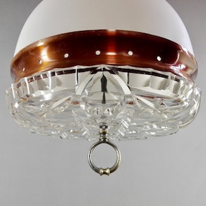 Könnte beinhalten: Eine Vintage-Pendelleuchte mit weißem Glasschirm, kupferfarbenem Band und dekorativer Kristallglasbasis. Die Leuchte hat einen Metallring zum Aufhängen.