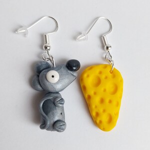 Peut inclure: Une paire de boucles d'oreilles pendantes argentées avec une souris grise et un morceau de fromage jaune.