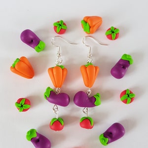 Peut inclure: Une paire de boucles d'oreilles pendantes avec un charme d'aubergine violette, de poivron orange et de tomate rouge. Les boucles d'oreilles sont en pâte polymère et ont des crochets argentés.