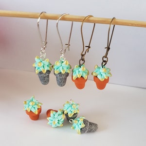 Peut inclure: Un ensemble de six boucles d'oreilles en pâte polymère faites à la main. Les boucles d'oreilles présentent de petites succulentes vertes dans des pots en terre cuite et gris avec des accents dorés. Les boucles d'oreilles sont sur des crochets argentés et bronze.