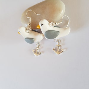 May include: A pair of silver dangle earrings featuring white and gray bird charms with silver anchor charms hanging below.
