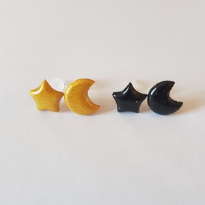 Puede incluir: Un par de pendientes de estrella y media luna de color dorado y negro. Los pendientes están hechos de arcilla polimérica y tienen un acabado brillante.