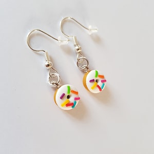 May include: A pair of silver dangle earrings with white donut charms decorated with colourful sprinkles.