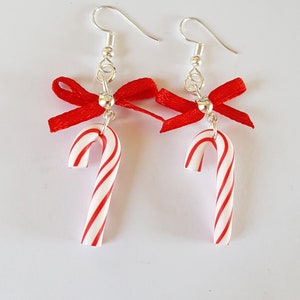 Peut inclure: Une paire de boucles d'oreilles pendantes argentées avec des nœuds rouges et des breloques de cannes en sucre blanc et rouge.