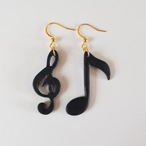 Könnte beinhalten: Ein Paar schwarze Ohrhänger mit einem Violinschlüssel und einer Note. Die Ohrringe haben goldene Haken.