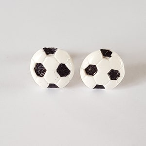 May include: A pair of small, white and black football stud earrings.