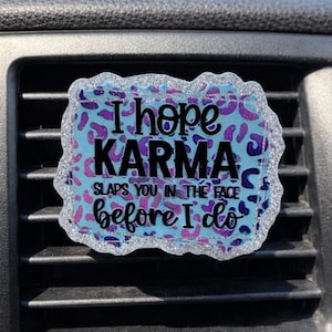 May include: A rectangular car air vent accessory with a glittery silver border. The center features a blue background with purple leopard print and the text "I hope KARMA slaps you in the face before I do."