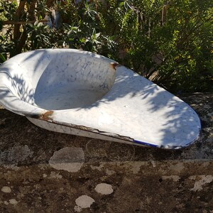 May include: A white enamelware basin with blue flecks and a blue rim. The basin is slightly chipped and has a rustic look.