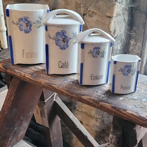 May include: Four white ceramic canisters with blue and yellow floral designs and blue stripes. The canisters are labelled "Farine", "Café", "Epices", and "Poivre".