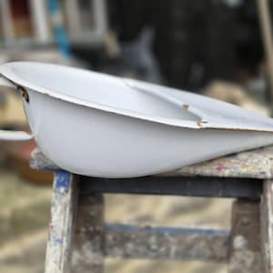 May include: White enamelware chamber pot with a handle. The chamber pot is sitting on a wooden stool with paint splatters.