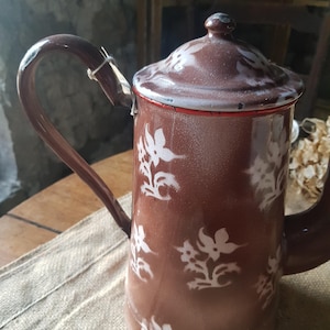 May include: A brown enamel teapot with a white floral pattern. The teapot has a red rim and a white lid.