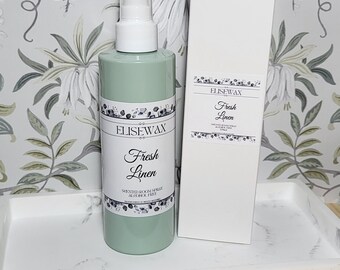 May include: A green glass bottle with a white spray nozzle and a white label that says "Elisewax Fresh Linen Scented Room Spray Alcohol Free". The bottle is sitting on a white tray with a white background.