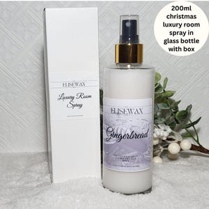 Może przedstawiać: Szklana butelka o pojemności 200 ml z odświeżaczem powietrza o zapachu piernika, z białą etykietą i złotą nakrętką. Butelka znajduje się w białym pudełku z napisem "ELISEWAX Luxury Room Spray" na etykiecie. Butelka stoi na białym tle z gałązką białych jag&oacute;d.