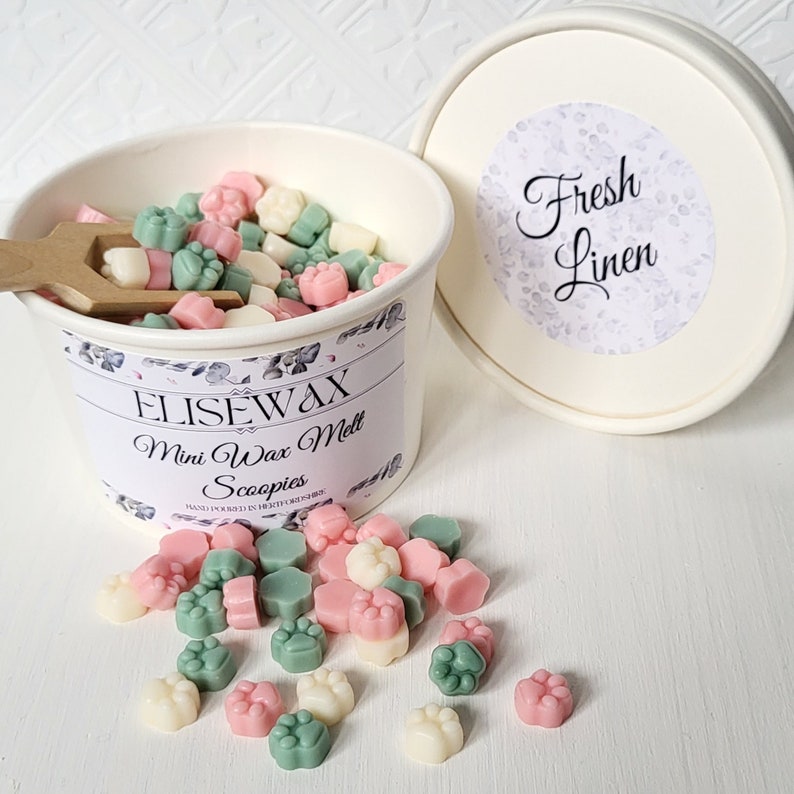 K&ouml;nnte beinhalten: Ein wei&szlig;er Beh&auml;lter gef&uuml;llt mit kleinen, bunten Wachs-Schmelzen in Form von Pfotenabdr&uuml;cken. Der Beh&auml;lter hat ein Etikett mit der Aufschrift "Elisewax Mini Wax Melt Scoopies" und "Hand Poured in Heart of the Home". Der Deckel des Beh&auml;lters hat einen Aufkleber mit der Aufschrift "Fresh Linen".