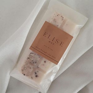 May include: A package of Elise Wax, Oud Mirage scented wax melts. The wax melts are in a clear plastic wrapper with a brown label. The label reads "ELISE WAX" and "Hand Poured | Est 2021". The wax melts have a speckled appearance.