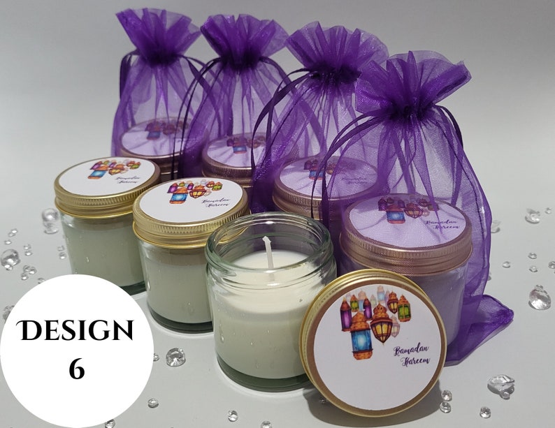 May include: Six small glass jars with gold lids and labels that say "Ramadan Kareem" in a decorative font. The jars are filled with white candles and are sitting on a purple sheer fabric.