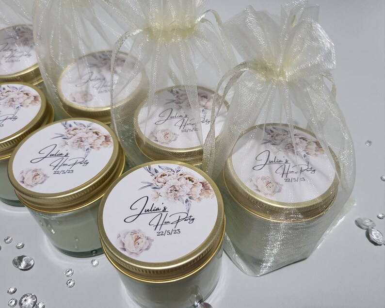 Puede incluir: Un conjunto de seis peque&ntilde;os frascos de vidrio con tapas doradas y etiquetas florales. Las etiquetas dicen "Julia's Hen Party 22/5/23". Los frascos est&aacute;n envueltos en bolsas de organza dorada transparentes.