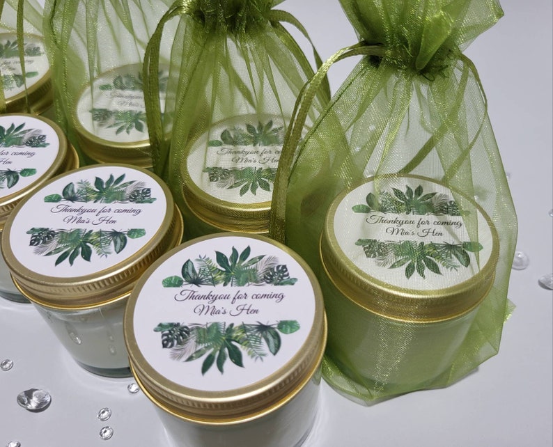 Puede incluir: Peque&ntilde;os frascos de vidrio con tapas doradas y etiquetas verdes y blancas que dicen "Thankyou for coming Mia's Hen". Los frascos est&aacute;n en bolsas de organza verde.