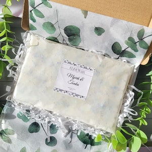 K&ouml;nnte beinhalten: Ein rechteckiges Paket Duftwachs, beschriftet mit "Myrrh & Tonka" von EliseWax, liegt in einer Pappschachtel. Das Wachs ist wei&szlig; mit blauen Sprenkeln und in Seidenpapier mit gr&uuml;nen Eukalyptusbl&auml;ttern verpackt.
