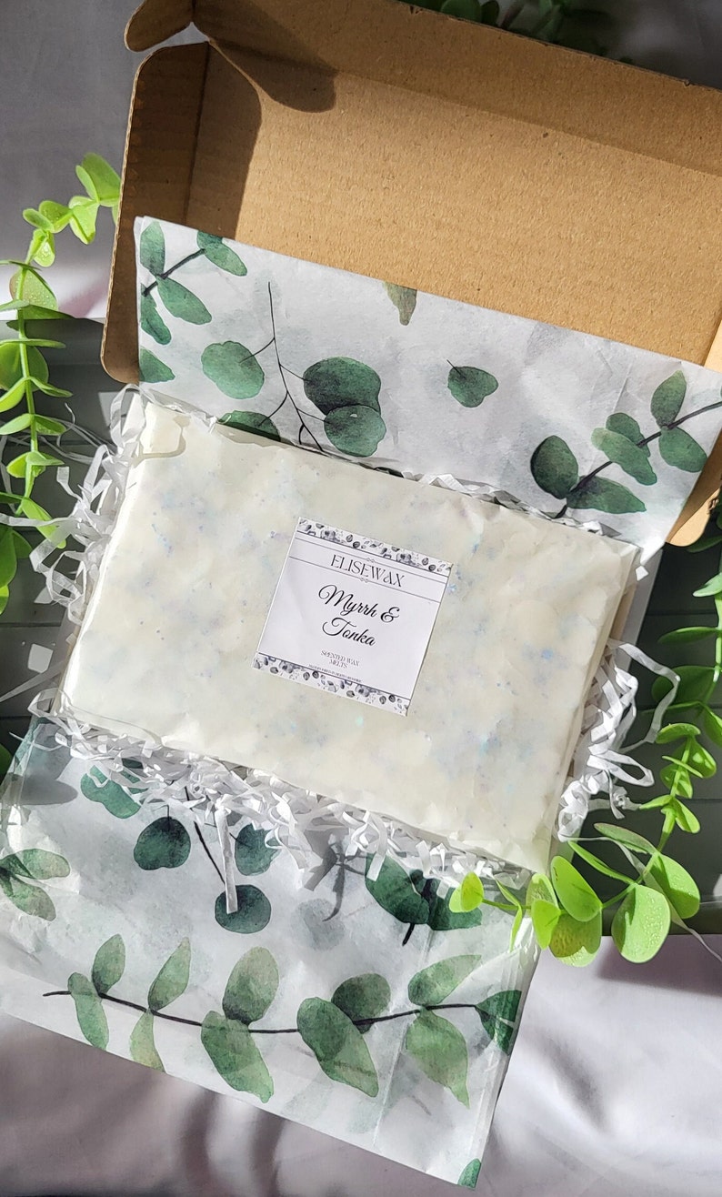K&ouml;nnte beinhalten: Ein rechteckiges Paket Duftwachs, beschriftet mit "Myrrh & Tonka" von EliseWax, liegt in einer Pappschachtel. Das Wachs ist wei&szlig; mit blauen Sprenkeln und in Seidenpapier mit gr&uuml;nen Eukalyptusbl&auml;ttern verpackt.