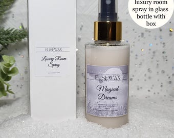 May include: A white box with a label that reads "ELISEWAX Luxury Room Spray" next to a glass bottle of room spray with a gold lid and label that reads "ELISEWAX Magical Dreams". The bottle is sitting on a white, sparkly surface.