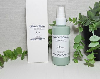 May include: A green spray bottle and a white box with the text "Roses" and "ELISEWAX" on the labels. The labels have a floral design. The spray bottle is next to a white box. The background includes a plant in a black pot.