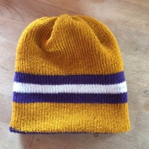 May include: A gold knit beanie with a white and purple stripe.