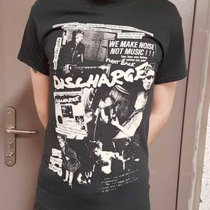 Puede incluir: Camiseta negra y blanca de la banda Discharge con un collage de im&aacute;genes y texto. El texto incluye "We make noise not music!!!" y "Fight Back".