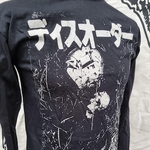 K&ouml;nnte beinhalten: Schwarzes Langarmshirt mit einem wei&szlig;en Grafikdruck eines Gesichts mit dem Text "ディスオーダー パーディション" in Japanisch.