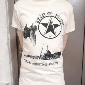 May include: A white t-shirt with a black and white graphic print. The graphic features a pentagram with a peace sign inside, a winged demon, and the text "Icons of  Elite" and "Onward Christian Soldiers".