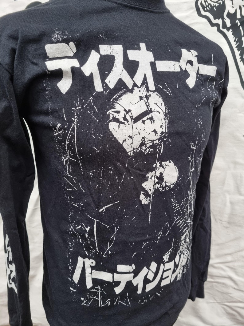 K&ouml;nnte beinhalten: Schwarzes Langarmshirt mit einem wei&szlig;en Grafikdruck eines Gesichts mit dem Text "ディスオーダー パーディション" in Japanisch.