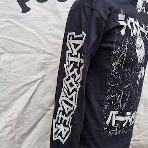 K&ouml;nnte beinhalten: Schwarzes Langarmshirt mit wei&szlig;em Text auf den &Auml;rmeln und dem R&uuml;cken. Der Text auf den &Auml;rmeln lautet "DISCHARGE" und der Text auf dem R&uuml;cken lautet "Discharge" in japanischen Schriftzeichen und "パーディション" in japanischen Schriftzeichen.