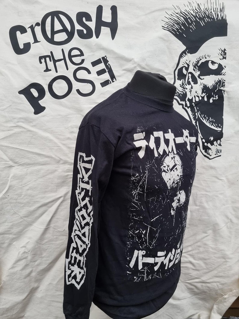 K&ouml;nnte beinhalten: Schwarzes Langarmshirt mit wei&szlig;em Druck. Die Vorderseite des Shirts zeigt eine Grafik einer Person mit dem Text "ライオター パーティション" in Japanisch. Der linke &Auml;rmel hat den Text "DESTROYERS" in wei&szlig; gedruckt.