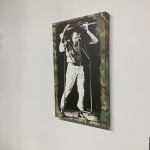 Op de afbeelding: Een zwart-witfoto van een muzikant die op het podium optreedt. De foto is afgedrukt op een canvas met een camouflage rand.