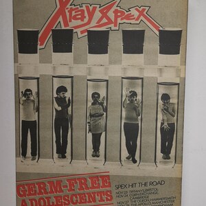 Pu&ograve; includere: Una copertina di un album vintage della band X-Ray Spex. La copertina presenta una grafica rossa e bianca del nome della band. Cinque membri della band sono ritratti in provette, con il titolo dell'album "Germ-Free Adolescents" e le date del tour elencate di seguito.
