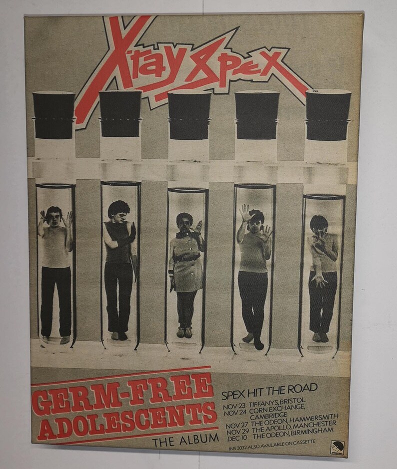 Pu&ograve; includere: Una copertina di un album vintage della band X-Ray Spex. La copertina presenta una grafica rossa e bianca del nome della band. Cinque membri della band sono ritratti in provette, con il titolo dell'album "Germ-Free Adolescents" e le date del tour elencate di seguito.