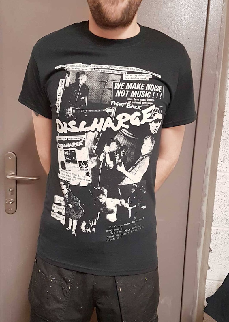Puede incluir: Camiseta negra y blanca de la banda Discharge con un collage de im&aacute;genes y texto. El texto incluye "We make noise not music!!!" y "Fight Back".