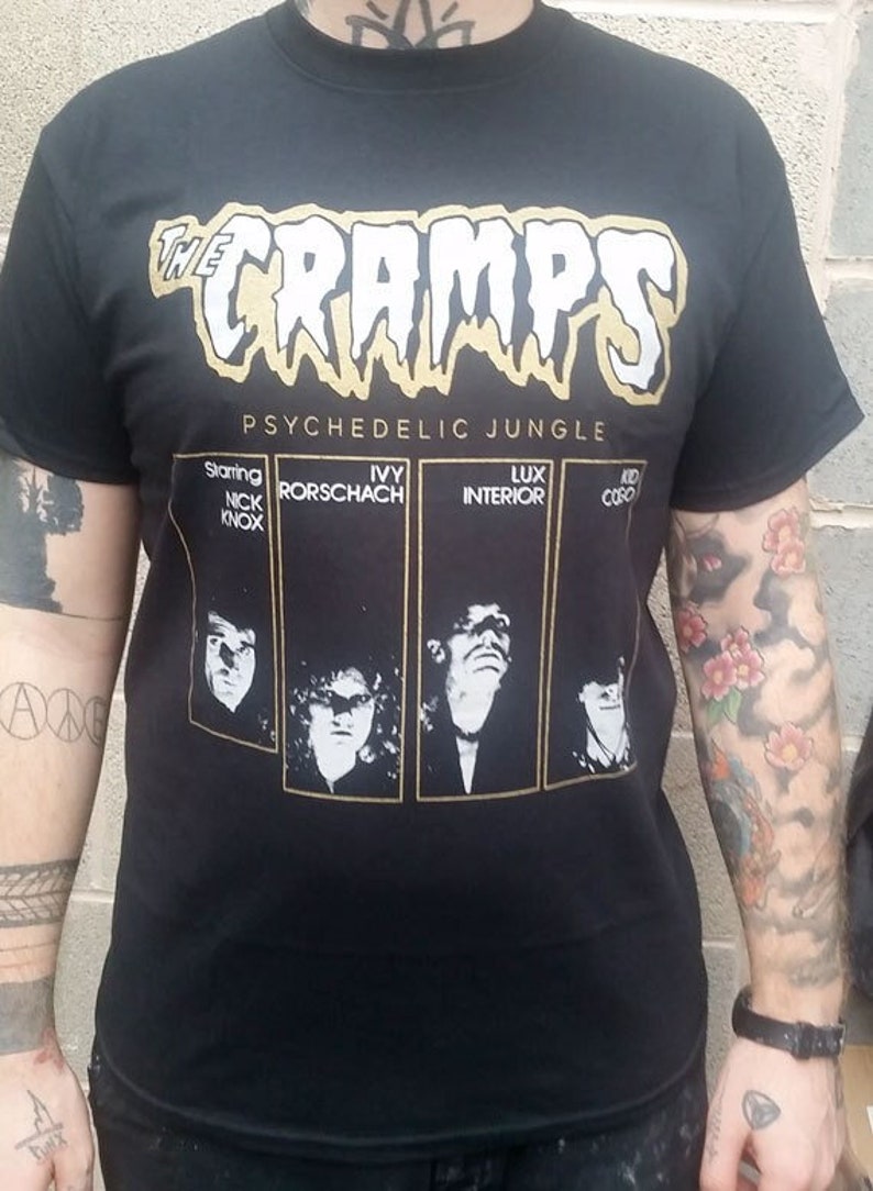 Puede incluir: Camiseta negra con un gr&aacute;fico blanco de "The Cramps" en una fuente que gotea con el texto "Psychedelic Jungle" debajo. La camiseta presenta cuatro fotos en blanco y negro de miembros de la banda con sus nombres debajo de cada foto: Nick Knox, Ivy Rorschach, Lux Interior y Kid Congo.