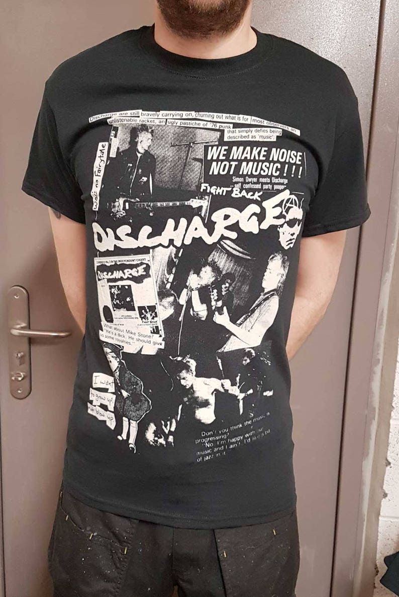 Puede incluir: Camiseta negra con un estampado gr&aacute;fico blanco de la banda de punk rock Discharge. El gr&aacute;fico incluye el nombre de la banda, una foto de los miembros de la banda y el texto "We Make Noise Not Music!!!" y "Fight Back".
