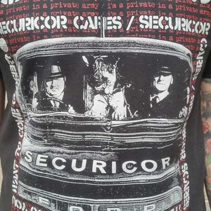 May include: Black and white graphic t-shirt featuring a band called "CRASS" with the text "SECURICOR OR CAGES / SECURICOR?" and a black and white image of a car with two people and a dog inside.