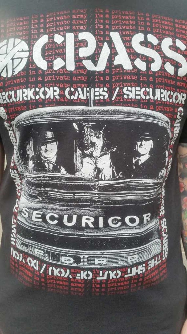 May include: Black and white graphic t-shirt featuring a band called "CRASS" with the text "SECURICOR OR CAGES / SECURICOR?" and a black and white image of a car with two people and a dog inside.