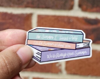 Könnte beinhalten: Ein Aufkleber mit einem Stapel von drei Büchern. Die Titel lauten "The Summer I Turned Pretty", "It's Not Summer Without You" und "We'll Always Have Summer". Die Buchumschläge sind pastellblau, pfirsichfarben und lila.