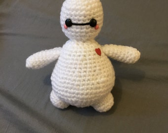 May include: White crocheted plush toy resembling a robot with black eyes, a black mouth, and a red heart on its chest.