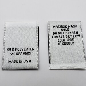 May include: Two white fabric care labels with black text. The label on the left reads "95% Polyester 5% Spandex Made in U.S.A.". The label on the right reads "Machine Wash Cold Do Not Bleach Tumble Dry Low Cool Iron If Needed".