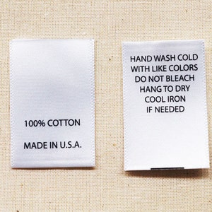 May include: Two white fabric labels with black text. The label on the left says "100% COTTON MADE IN U.S.A.". The label on the right says "HAND WASH COLD WITH LIKE COLORS DO NOT BLEACH HANG TO DRY COOL IRON IF NEEDED".