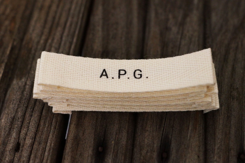 May include: A stack of white fabric labels with the text "A.P.G." printed in black.