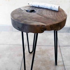 May include: A small, round wooden side table with a natural wood grain finish. The table has three black hairpin legs and a decorative pencil on top. The table is approximately 46 cm in diameter.