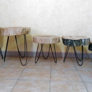 Peut inclure: Ensemble de cinq tables d'appoint en bois. Chaque table est composée d'un plateau en tranche de bois naturel et de pieds en épingle noirs. Les tables varient en taille, la plus grande mesurant environ 46 cm de diamètre, et la plus petite environ 30 cm.