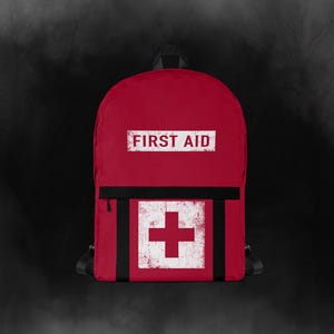 Peut inclure: Un sac à dos rouge avec l'inscription "FIRST AID" dans un rectangle blanc. En dessous, une croix blanche dans un carré rouge est centrée sur le devant. Le sac à dos a des bretelles noires et une fermeture éclair noire.